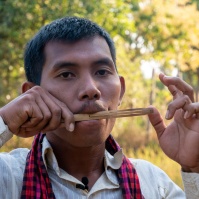 CHI Monivong playing Angkuoch Russey (bamboo Jew’s harp). (Photo: Catherine Grant, 6 January 2020)  •  លោក ជី មុនីវង់ ផ្ទាត់អង្កួចឬស្សី។ រូបថតដោយ៖ ខាត់ធឺរីន ហ្ក្រាន, ថ្ងៃទី ០៦ ខែមករា ឆ្នាំ២០២០​។