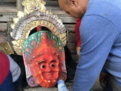 A man leads a toddler to a mask which has been taken off by a dancer who is resting during a local festival, Ganesh Temple, Yecce, Nepal. Photo: Renuka Gurung.