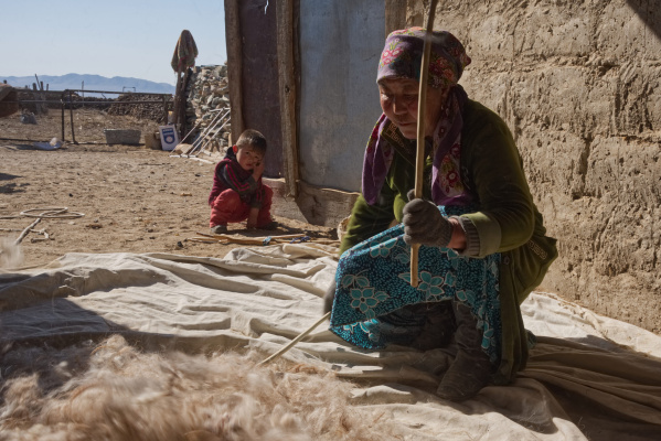A woman prepares wool for feltmaking while her grandson looks on. Photo: Bob Glennan
